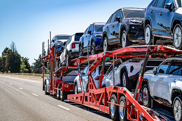 A red TX Auto Transport Fort Worth truck carries multiple new cars on two levels along a highway under a clear blue sky.